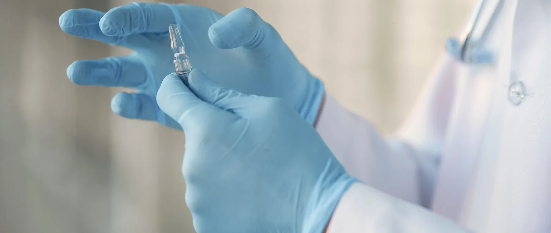 Close-up of a healthcare professional in gloves holding a glass vaccine ampoule.