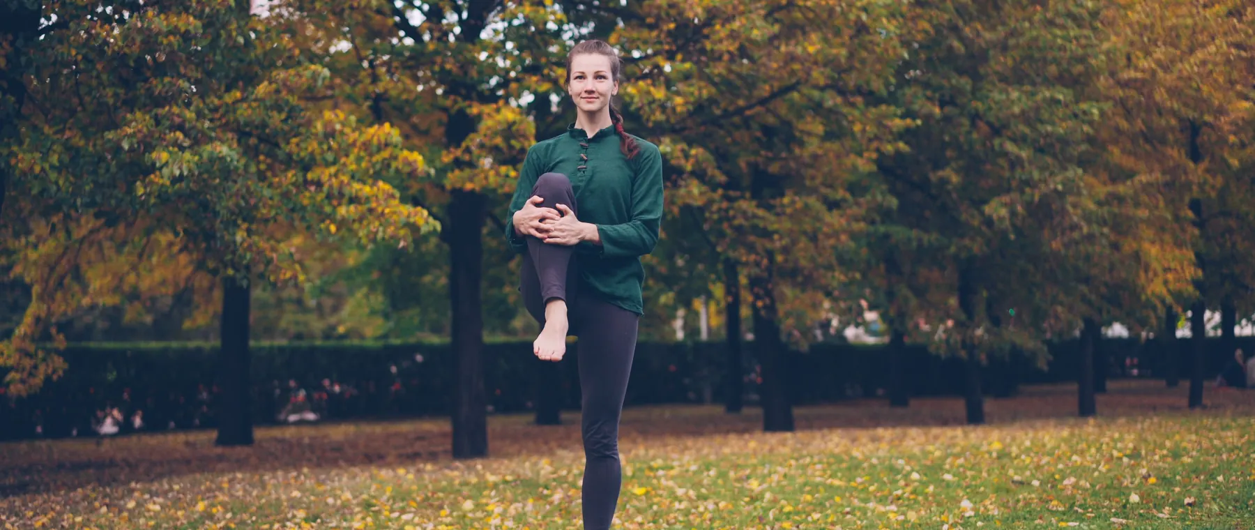 A woman practicing yoga on a mat in a park surrounded by autumn trees, promoting outdoor fitness.