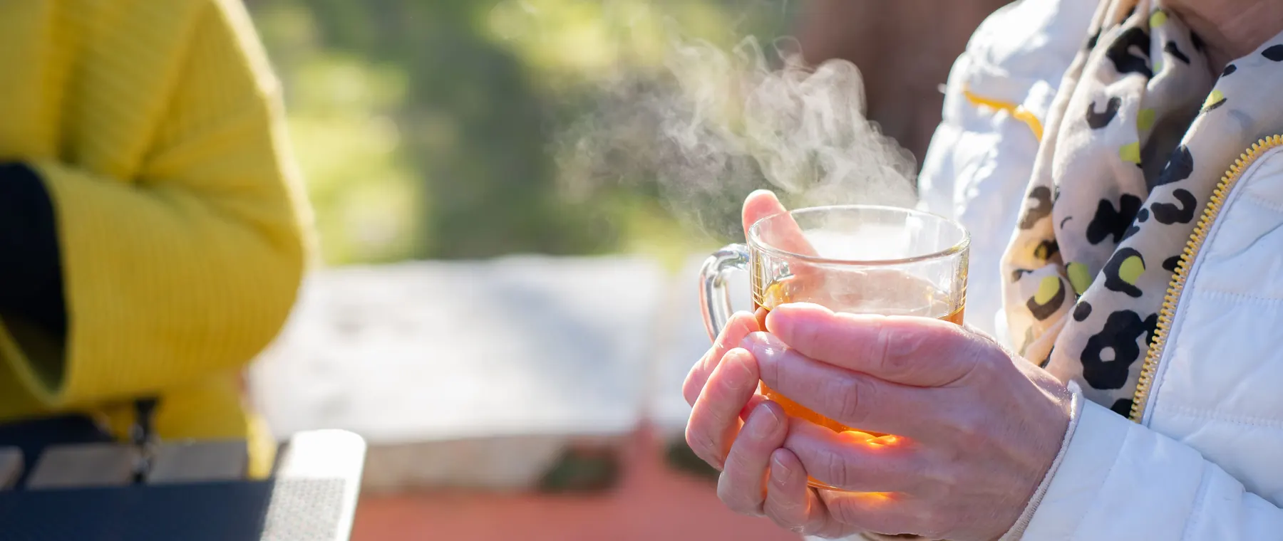 Elderly woman savoring hot tea outdoors, capturing warmth and relaxation in natural setting.