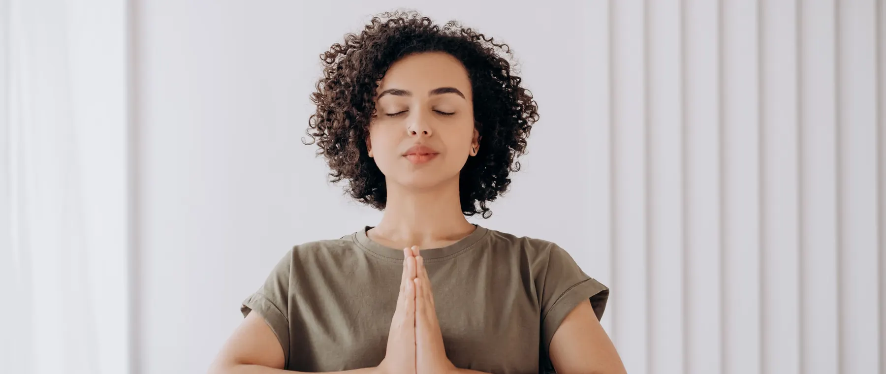Young woman with curly hair meditates indoors, embracing tranquility and mindfulness.