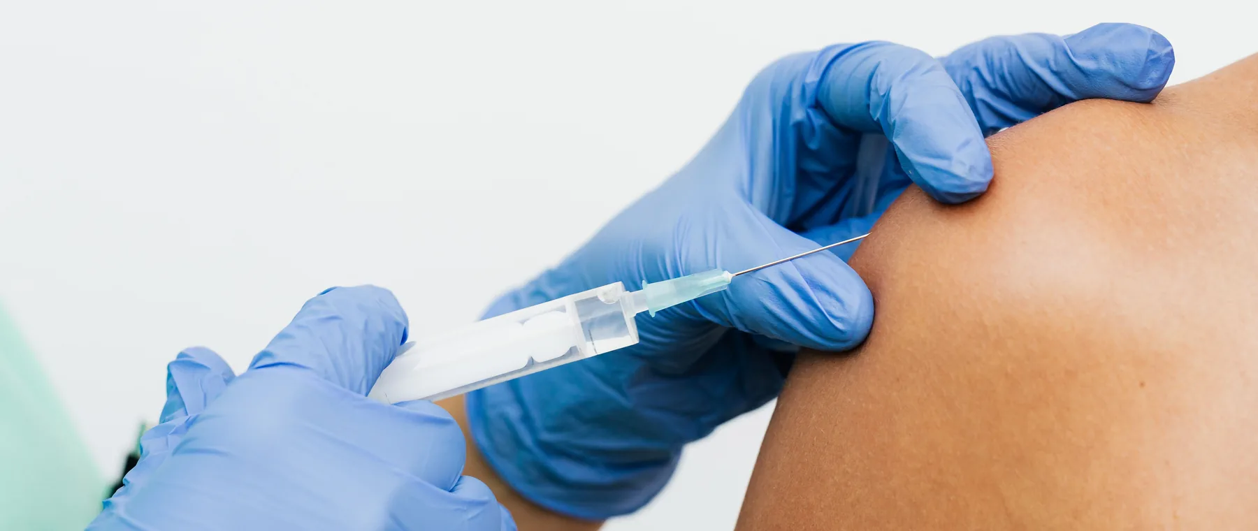 A gloved clinician placing an injection into a shoulder muscle