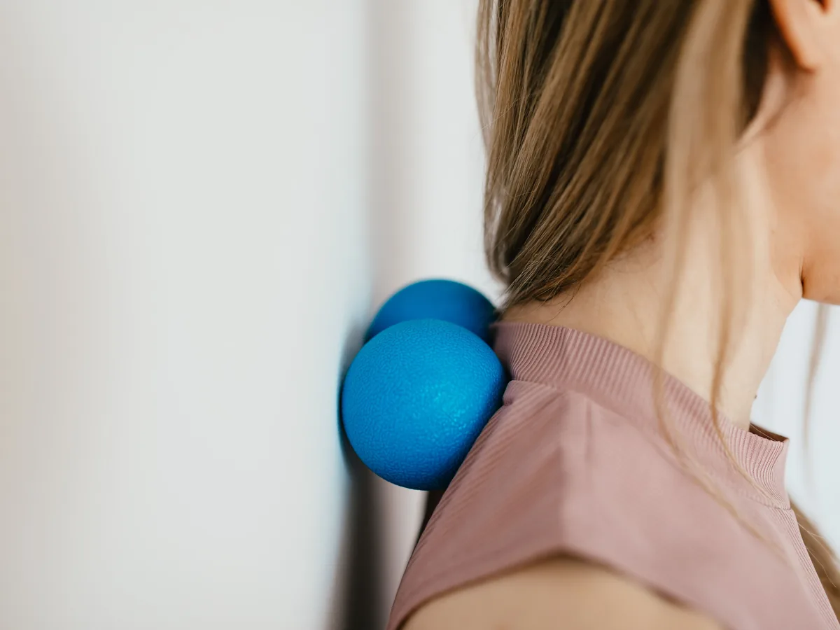 Side view crop unrecognizable female leaning on small balls against wall to massage stiff neck muscles and sore neck