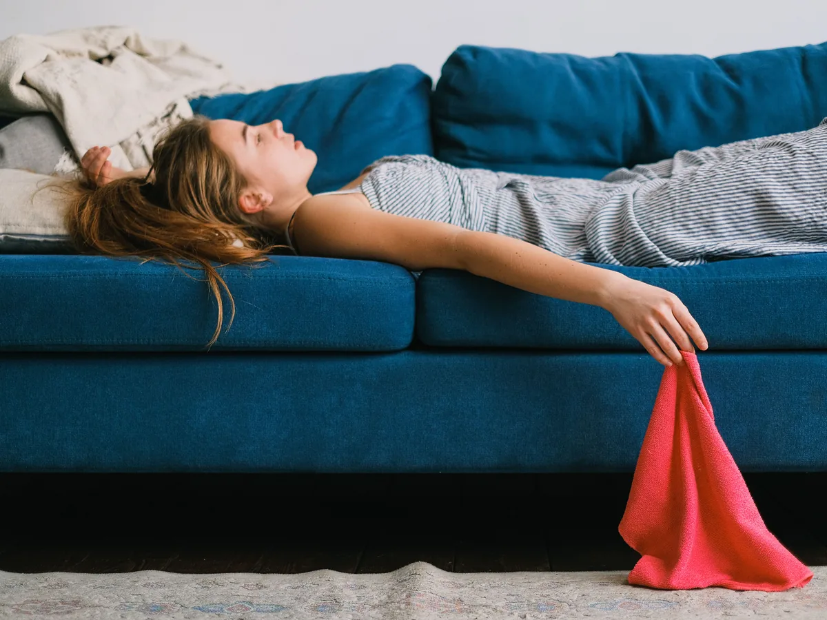 Side view of young exhausted woman with rag lying on couch in living room in daylight