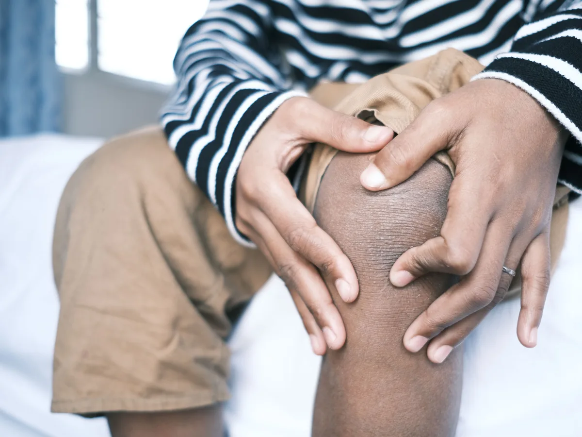 Close-up of a person holding their knee, highlighting skin texture and striped clothing.