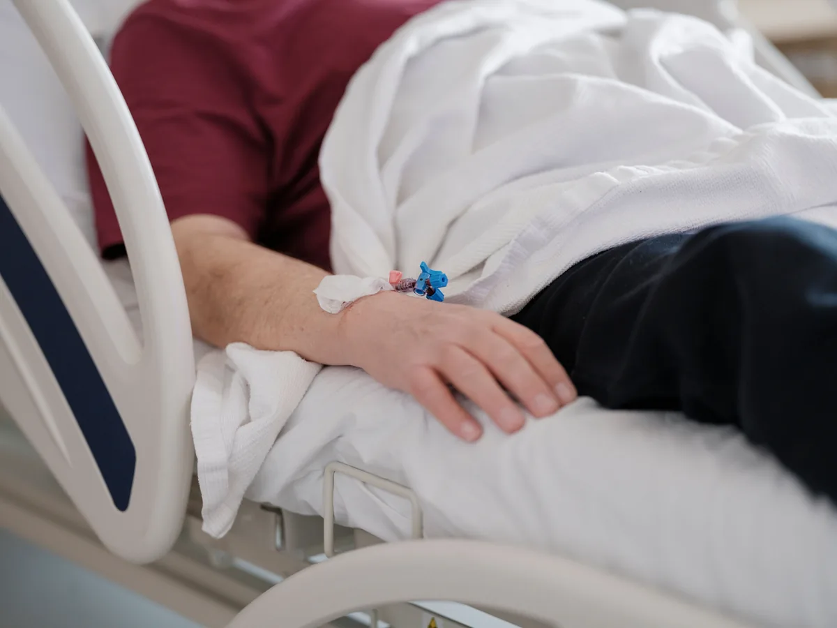 Close-up of a patient's hand with an IV drip lying on a hospital bed.