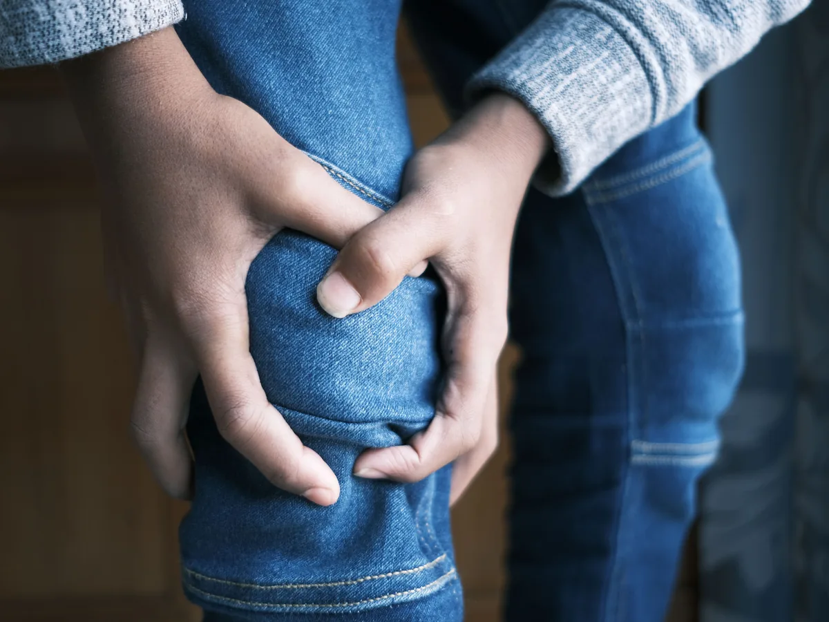 Close-up image of hands holding a knee in jeans, indicating pain or injury.