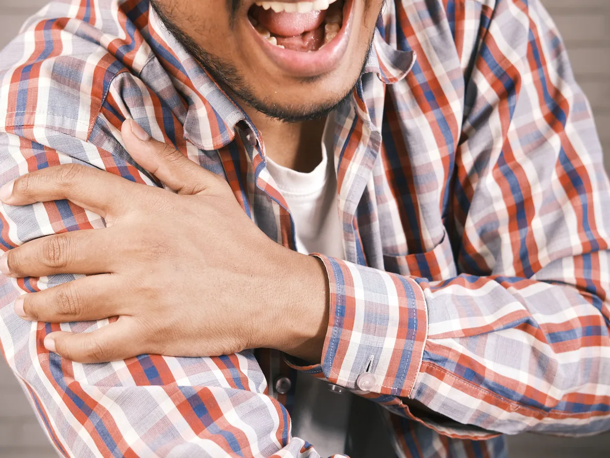 Close-up of a man in plaid shirt experiencing shoulder pain, grasping his arm.