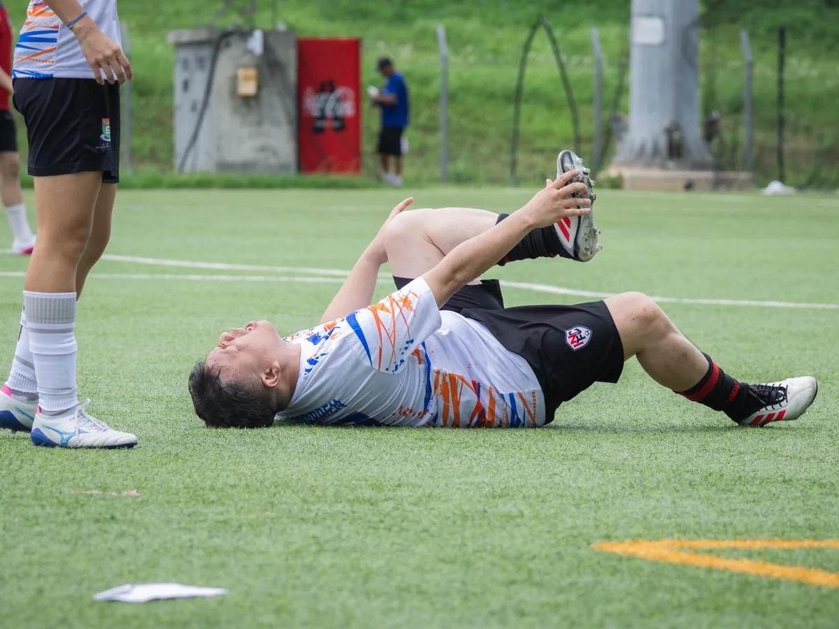 A soccer player lies on the field with an apparent leg injury during a game, needing assistance.