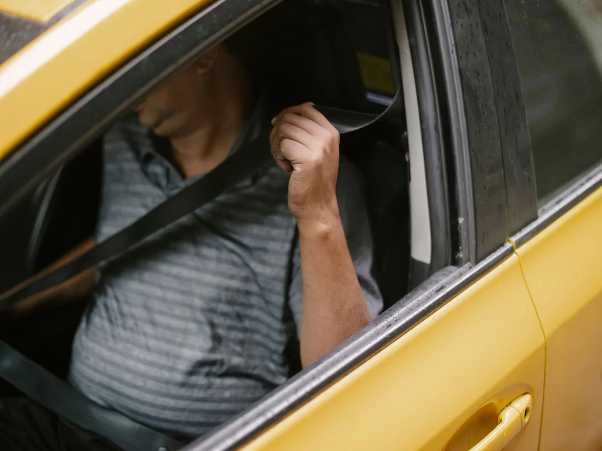 High angle of anonymous middle aged man in casual clothes fastening seat belt before riding yellow taxi parked on street