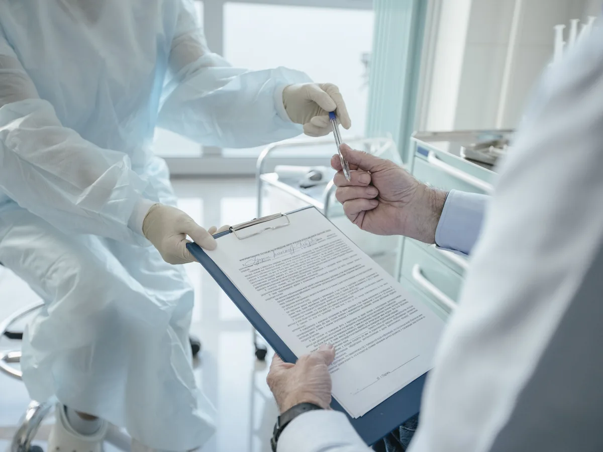 A clinician handing a clipboard to a patient to sign