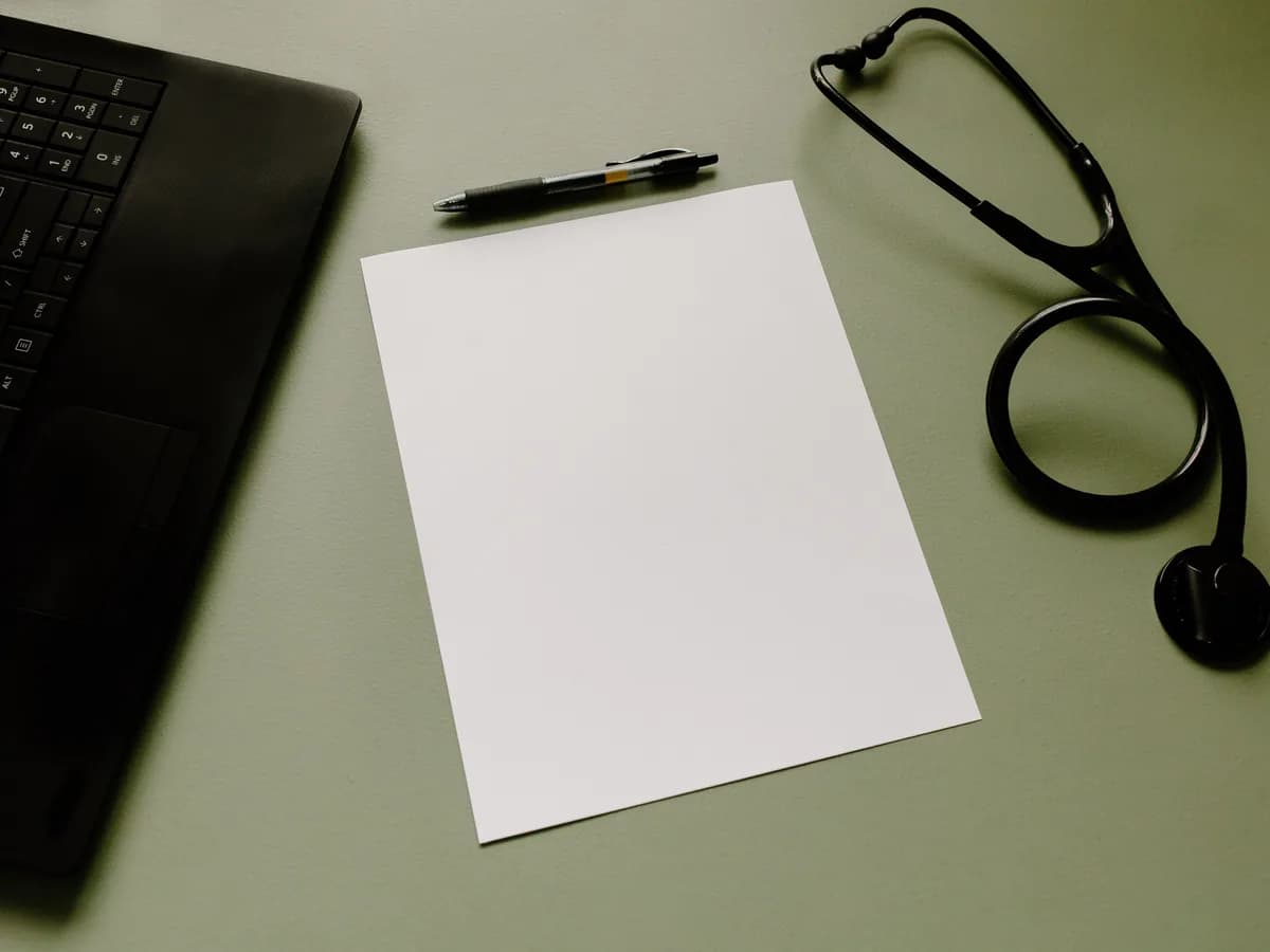 A clinician workspace with a stethoscope, notes and laptop