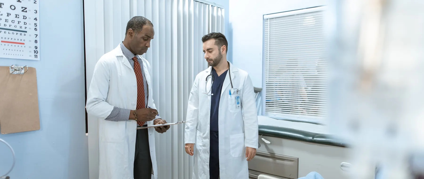 Two doctors review a patient's chart in a hospital room, focusing on healthcare cooperation and medical care.