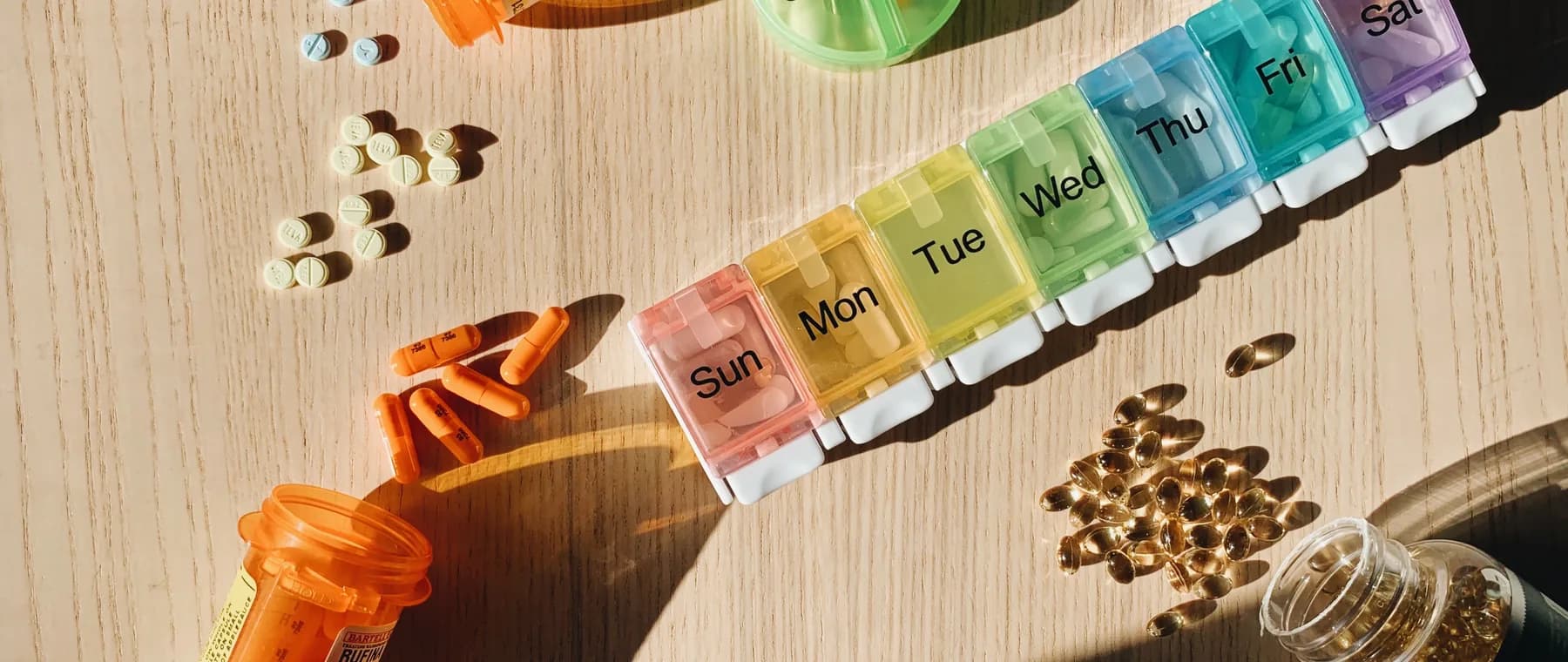 A weekly pill organiser and medication bottles laid out on a table