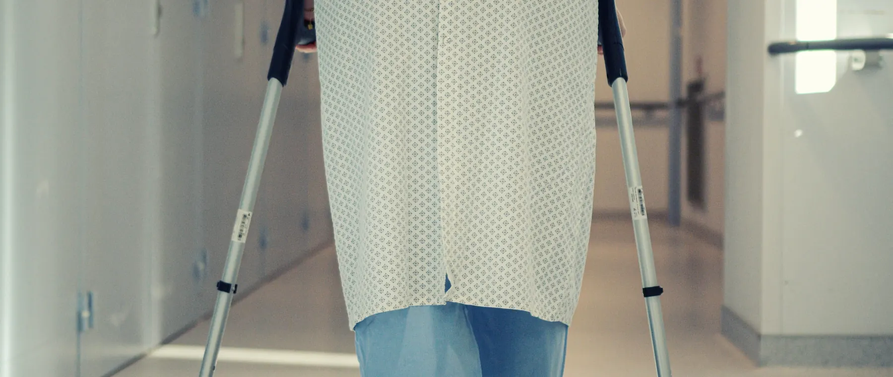 A senior patient using crutches to walk down a hospital corridor, symbolizing recovery and mobility assistance.