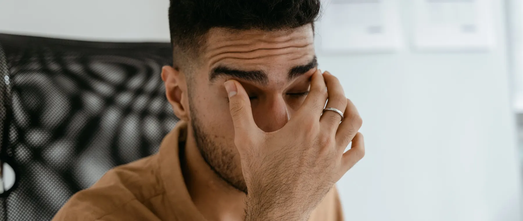 Close-up of a man rubbing his eyes, capturing stress or fatigue in an office environment.